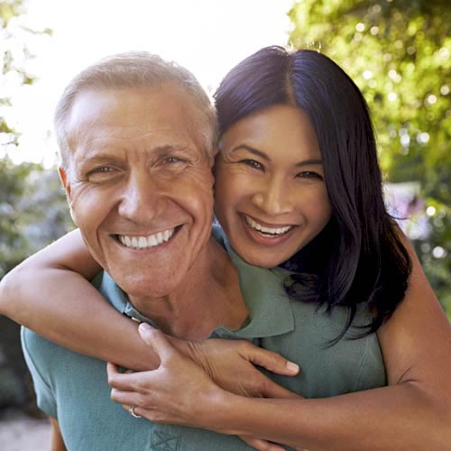 A woman hugs a man from behind, both are smiling